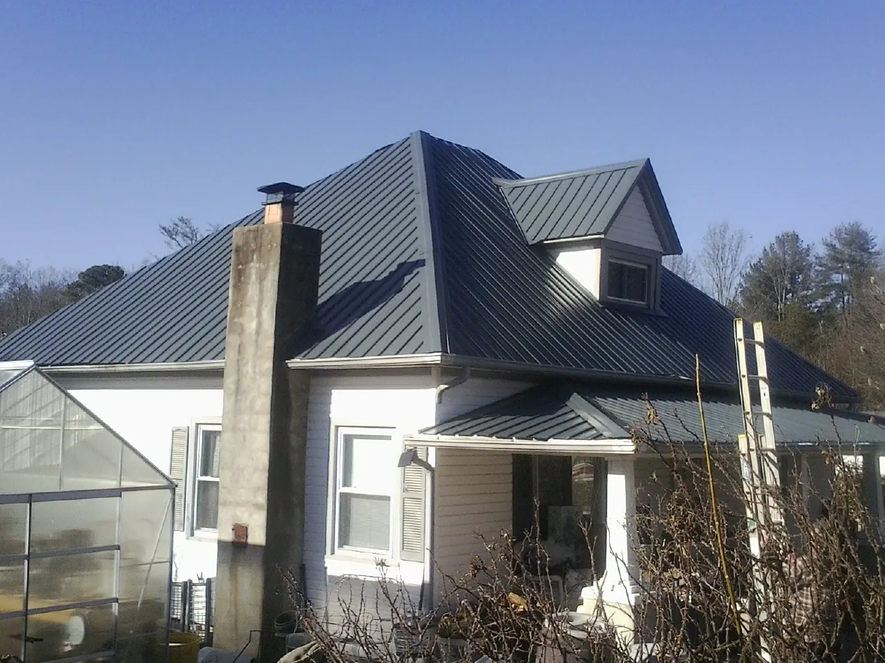 Dark blue standing seam metal roof on a white farmhouse with dormer — Slate & Tile Roof Repair by Roofing Brothers in Greendale