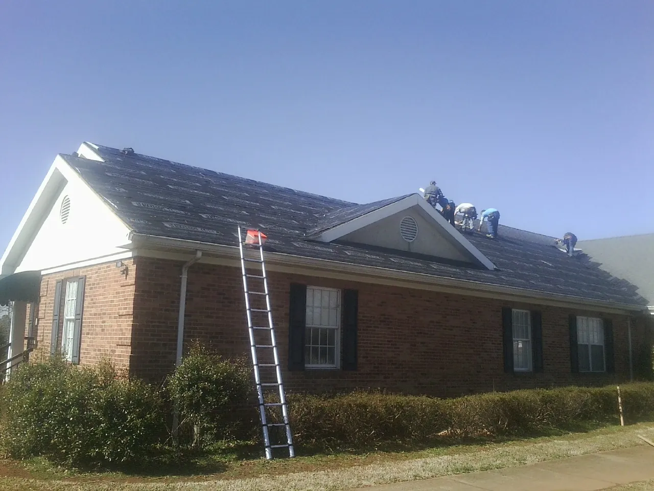 Crew tearing shingles off a brick ranch roof with a ladder set — Emergency Roof Repair work by our crew in Greendale