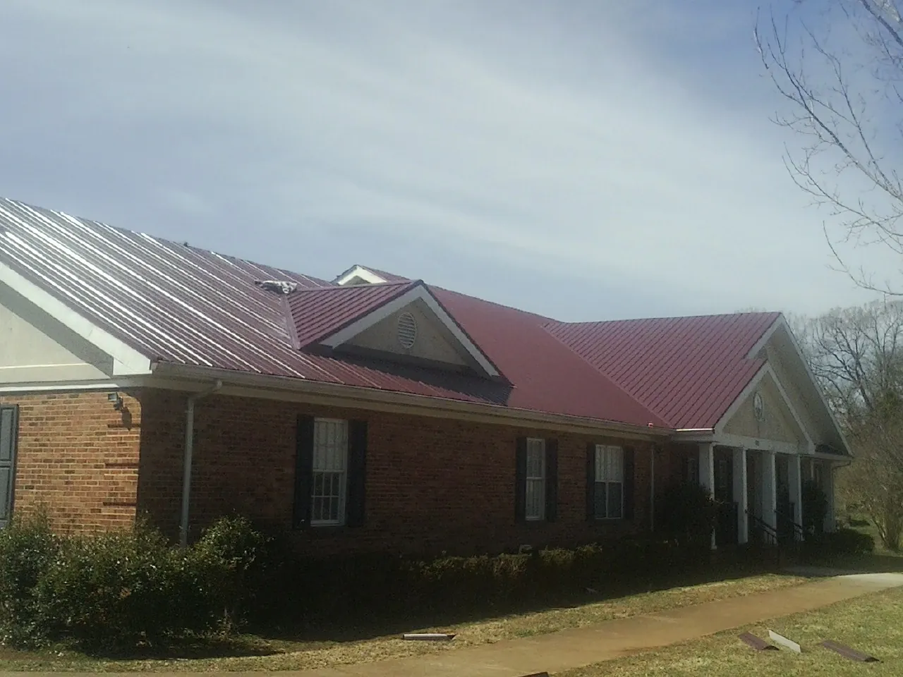Red metal roof with gabled entries on a long brick building, from a Hail Damage Roof Repair job in Greendale