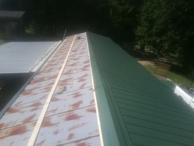 Old rusted panels beside newly installed green metal roofing — Wind Damage Roof Repair by Roofing Brothers in Greendale