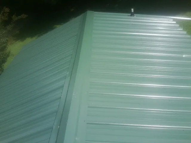 New green metal panels meeting at the ridge of a roof — Flat Roof Repair work by our crew in Greendale