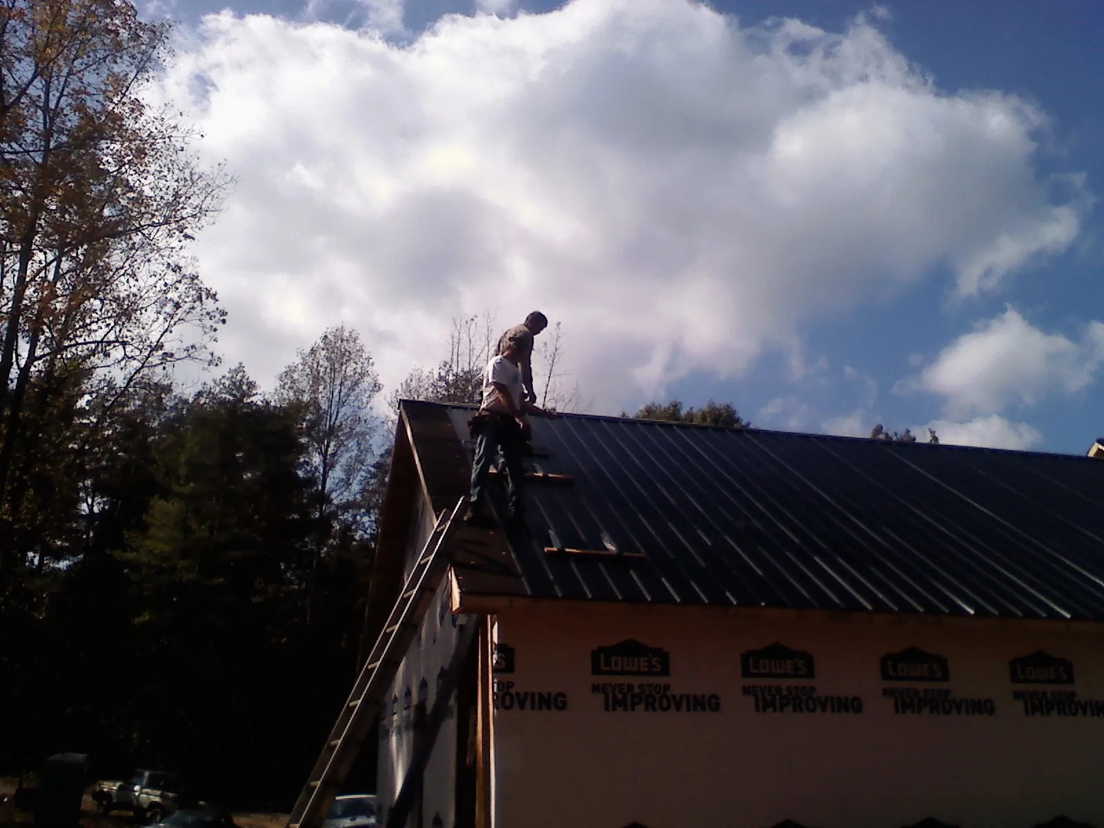 Roofer fastening dark metal panels high against a cloudy sky, from a Roof Inspection job in Greendale