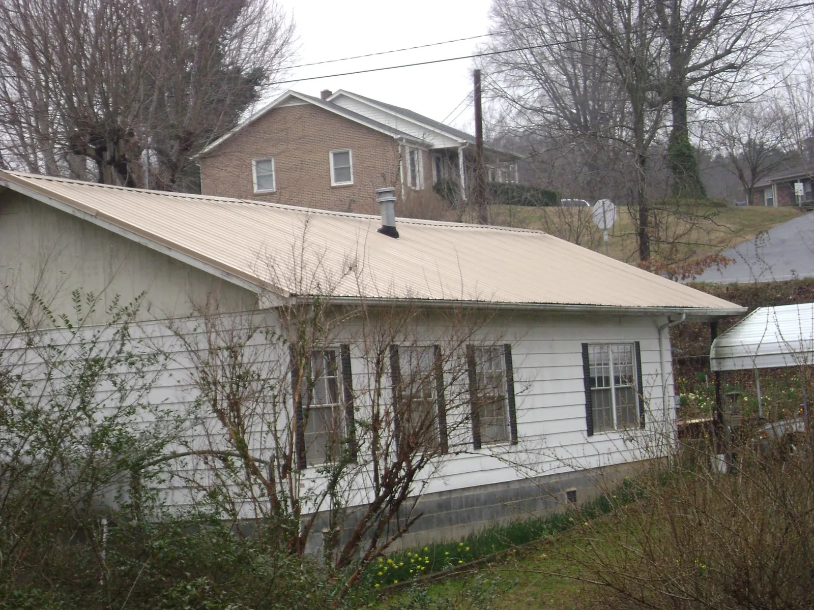 Tan metal roof on a white sided house set into a hillside — Commercial Roofing by Roofing Brothers in Greendale
